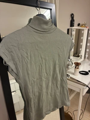 Grå ribbad polotopp - Snygg grå polotopp med ribbad struktur och ärmlös design. Perfekt att styla med jeans eller kjol för en trendig look. Hög krage ger en cool vibe och passar till många outfits.