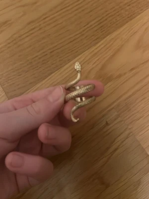 Guldig ormring i metall - Unik ring i form av en orm som slingrar sig runt fingret. Ringen är guldfärgad och har detaljerad struktur som liknar ormens fjäll. Perfekt statement piece för dig som vill sticka ut med dina accessoarer.