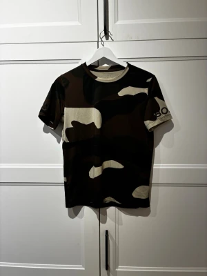 Camouflage t-shirt från Björn Borg - Cool t-shirt från Björn Borg med camouflage-mönster i svart, beige och brunt. Klassisk rund halsringning och korta ärmar. Perfekt för en avslappnad och sportig stil. Materialet är mjukt och skönt, troligtvis polyester. Nypris (300)