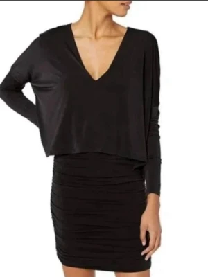 Svart långärmad klänning BCBG Max Azria - Stilren svart klänning från BCBG Max Azria med lång ärm och draperad kjoldel. Klänningen har en smickrande v-ringning och figurnära passform. Perfekt för dig som gillar klassisk och elegant stil.