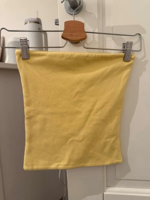 Gul axelbandslös tubtopp - Enkel och stilren ljusgul tubtopp i mjukt bomullstyg. Axelbandslös modell med rak passform som ger en clean och fräsch look. Perfekt att styla till jeans eller kjol för en somrig vibe.