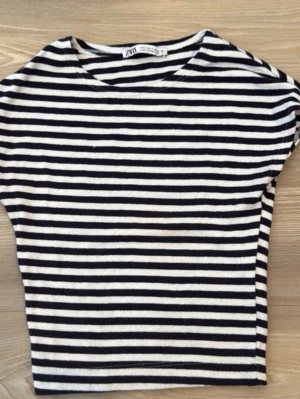 Randig topp från Zara i bomull - Snygg topp från Zara med klassiskt svartvitt randigt mönster. Modellen har rund halsringning och korta ärmar. Tillverkad i mjuk bomull som känns skön mot huden. Perfekt att styla med jeans eller kjol för en trendig look.