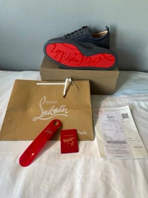 Christian Louboutin - Gråa sneakers från Christian Louboutin i mocka med ikoniska röda sulor och nitar på tån. Lågt skaft och klassisk snörning. Lyxig och edgy design som sticker ut med exklusiva detaljer och material.