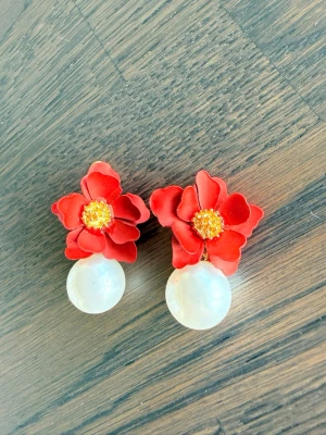 Röda blomörhängen med pärldetalj - Snygga örhängen med röda blommor  och guldfärgade detaljer i mitten. Under varje blomma hänger en stor vit pärla som ger en cool kontrast. Perfekta för dig som vill sticka ut med färg och unika detaljer. Ej använda ❤️