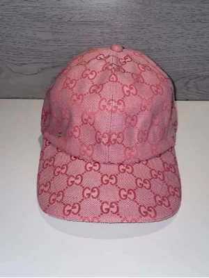 Rosa keps med mönster - Säljer en rosa keps med det klassiska monogrammet över hela kepsen. Kepsen har böjd skärm och är tillverkad i ett tygmaterial med en liten metallogo på sidan. Perfekt för dig som vill sticka ut med en lyxig accessoar.