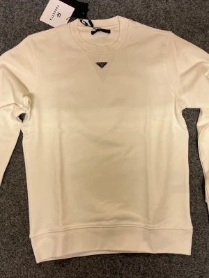 Vit sweatshirt från Prada - Snygg vit sweatshirt från Prada med diskret logga på bröstet. Tröjan har rund halsringning, långa ärmar och ribbade muddar vid ärmslut och nederkant. Tillverkad i mjukt material som känns skönt mot huden. Perfekt för en clean och stilren look.