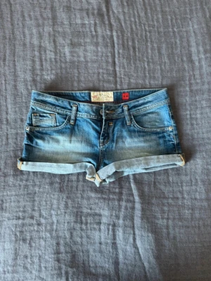 Blå denimshorts med låg midja - Snygga blå jeansshorts från QS by s.Oliver med låg midja. Perfekta för sommaren och sitter jätte bra. De är vintage och finns inte att köpa längre. Shortsen sitter som M/38.