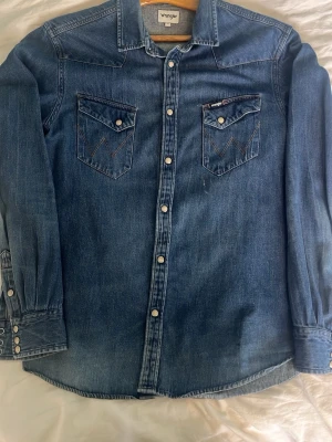 Vintage Denimskjorta  - Riktigt snygg denim skjorta med en mer slim passform. Sätter sig riktigt snyggt över armarna och bröstet. Den har snygga detaljer och den är av god kvalitet. Passar över en t-shirt eller själv med ett par snygga jeans. Skriv gärna för mer bilder!