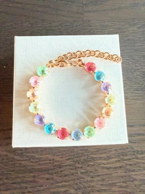 Armband med pastellfärgade stenar  - Fint armband med 8 mm stora glittriga stenar i olika pastellfärger som rosa, blå, grön, lila och gul. Stenarna  sitter i guldfärgad metall och armbandet har en justerbar kedja. Perfekt för dig som gillar färgglada accessoarer och vill sticka ut lite extra.