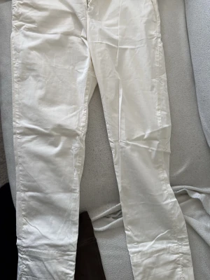 Vita byxor från HOPE - Snygga vita byxor från HOPE med rak passform och dragkedja fram. Byxorna är tillverkade i ett mjukt bomullstyg och har klassisk design med fickor. Perfekta för en clean och stilren look.