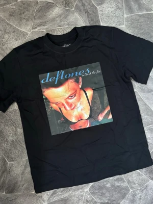 Deftones svart band t-shirt - Svart t-shirt med stort tryck av Deftones albumomslag 'Around the Fur' på bröstet. Klassisk rak passform och rund halsringning. Perfekt för dig som gillar alternativ rock och vill ha en statement tee.