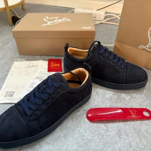 Mörkblå sneakers från Christian Louboutin - Snygga mörkblå sneakers från Christian Louboutin med klassisk röd sula och guldfärgad logga på insidan. Skorna har rund tå, platt sula och är tillverkade i mjuk mocka med skinnfoder. Perfekt för dig som gillar exklusiv stil och detaljer som sticker ut.