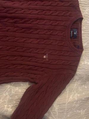 Vinröd stickad  tröja från Gant - Vinröd kabelstickad tröja från Gant i premium bomull. Tröjan har rund halsringning, ribbade muddar och Gant-logga broderad på bröstet. Perfekt för dig som gillar klassisk och stilren look.Skriv privat för mer bilder🤍
