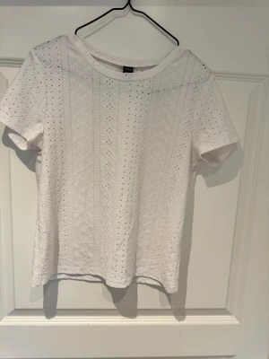 Vit spetsmönstrad t-shirt från SHEIN - Snygg vit t-shirt från SHEIN med korta ärmar och spetsmönster. Perfekt till jeans eller kjol för en fräsch look. Tillverkad i mjukt material som känns skönt mot huden.