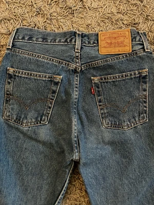 Levi's 534 blå raka jeans - Klassiska blå jeans från Levi's med raka ben och hög midja. Jeansen har två bakfickor med den ikoniska Levi's-sömmen och en brun läderpatch i midjan. Tillverkade i slitstark denim med en tidlös look.