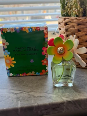 Daisy Wild Eau So Intense Marc Jacobs - Daisy Wild Eau So Intense från Marc Jacobs är en parfym i en genomskinlig glasflaska med färgglada blommor på locket. Förpackningen är grön med blommönster i flera färger. Flaskan rymmer 30 ml och har en lekfull och trendig design. Ny
