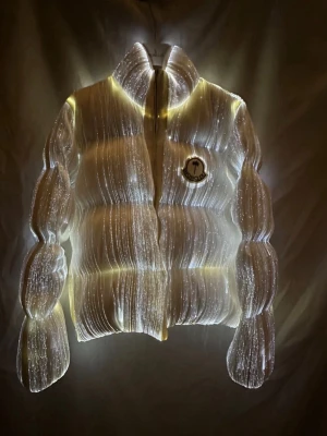 Vit pufferjacka från Moncler - Säljer en riktigt fet vit pufferjacka från Moncler med coolt reflekterande material som lyser i mörkret. Jackan har en hög krage, dragkedja och Moncler-logga på bröstet. Perfekt för dig som vill sticka ut i vinterkylan och hålla dig varm med stil.