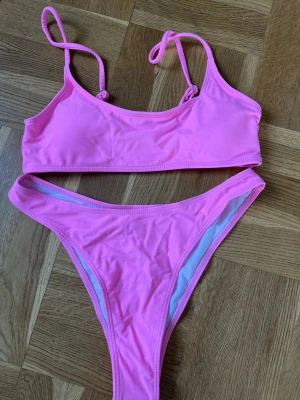 Rosa bikini med smala axelband - Snygg rosa bikini med smala axelband och enkel design från SHEIN. Bikinin har en sportig topp och klassiska bikinitrosor med hög midja. Klisterlappen i trosan är kvar, både topp och trosor är oanvända.