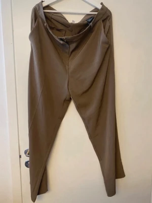 Bruna kostymbyxor från H&M - Snygga bruna kostymbyxor från H&M i rak modell, använd 1 gång men i väldigt bra skick. Storlek 50. 