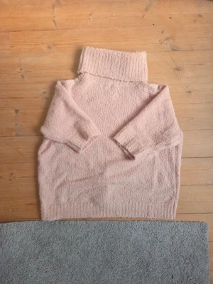 Ljusrosa stickad polotröja - Mysig ljusrosa stickad polotröja med oversized passform och bred polokrage. Tröjan har korta ärmad och är i stl M. Perfekt för kalla dagar när du vill vara både varm och snygg.