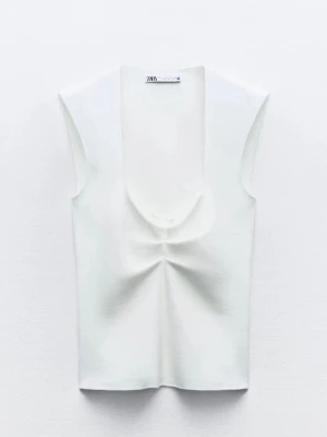 Vit topp från Zara - Snygg vit linnetopp från Zara med djup rundad urringning och ribbad struktur. Toppen är ärmlös och har en lätt croppad passform som ger en modern look. Perfekt att styla med jeans eller kjol för en trendig outfit.