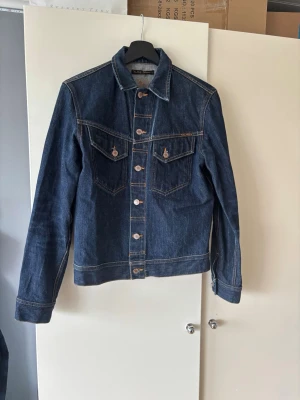 Mörkblå jeansjacka från Nudie Jeans - Klassisk mörkblå jeansjacka från Nudie Jeans med kontrastsömmar och två bröstfickor med knapp. Storlek S och i mycket gott skick! Hör av dig 🙌🤗