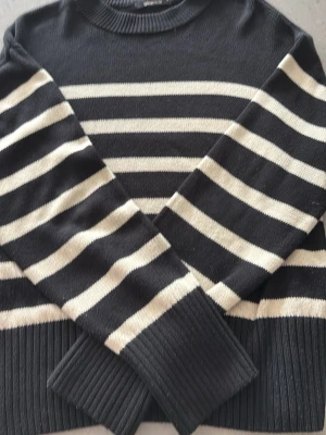 Svartvit randig stickad tröja Gina Tricot - Stickad tröja från Gina Tricot i svart och vitt med breda horisontella ränder. Tröjan har rund halsringning, långa ärmar och ribbade muddar vid ärmslut och nederkant. Perfekt för en avslappnad och trendig look.