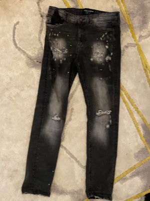 Svarta slitna skinny jeans - Säljer ett par svarta skinny jeans från Zara med slitningar och distressed detaljer på både fram- och baksida. Jeansen har en tvättad look med ljusare partier och små hål för en trendig, edgy stil. Perfekta för dig som gillar streetwear och vill sticka ut.