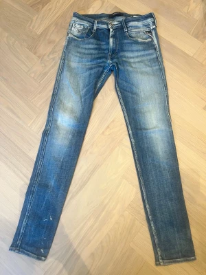 Replay anbass - Säljer ett par blå slim fit jeans med snygga slitningar och tvättade detaljer. Finns en mindre defekt på högra benet men annars bra skick. Storlek 32/34