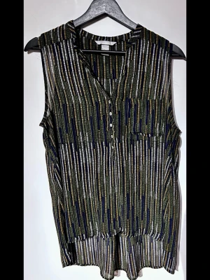  H&M mönstrad ärmlös blus (Stl 38) - Luftig mönstrad blus från H&M utan ärmar i stl 38 (M). Snygg henley-modell i 100% polyester med knappar fram, bröstficka och ett fint, längre fall baktill. Superfint skick utan anmärkningar.  Se sista bilden för måttband! Mått Bredd: ca 47cm, Axelbredd: ca 32cm, Längd: ca 74cm. Perfekt trendigt basplagg till garderoben! Skriv gärna vid frågor.