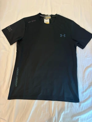 Under Armour träningsset – T-shirt + shorts - Säljer ett snyggt och funktionellt träningsset från Under Armour. Setet består av en snabbtorkande T-shirt och matchande shorts med resår och dragsko i midjan. Perfekt för gym, löpning, padel eller annan träning.  ✔️ Storlek: M ✔️ Skick: Helt nytt med prislappar kvar ✔️ Färg: Svart ✔️ Lätt, ventilerande och bekvämt material  Säljs som set. Hör gärna av dig om du har frågor eller vill ha fler bilder!