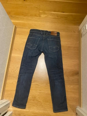 Mörkblå slim fit jeans från Replay - Säljer ett par mörkblå slim fit jeans från Replay med klassisk femficksdesign och snygga detaljer på bakfickorna. Jeansen har en metallknapp och dragkedja framtill samt Replay-logga på linningen. Storlek 29/32 men är lite mindre än så. Sitter som 28/30 ca