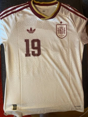 Spainen borta tröja vit bortatröja vm Lamine Yamal 19 - Nu ni! Jag har nog aldrig blivit så förvånad över hur snygg en tröja varit när jag fått hem de som över denna. Otroligt snygg med alla detaljer. Bra att ha en Spanien tröja inför vm finalen, eller?