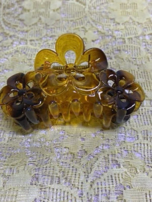 Brun hårklämma med blommor - Snygg hårklämma i transparent brun plast med blommönster och guldfärgad fjäder. Klämman har en klassisk form och detaljerade utskärningar som ger en retrovibe. Perfekt för att snabbt fixa frisyren och hålla håret på plats. Finns fler kvar , 