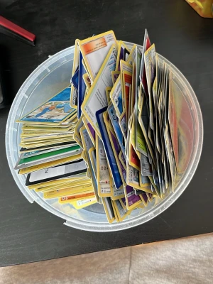 Stor samling Pokémonkort i plastburk - Säljer en stor blandad samling Pokémonkort i olika färger och motiv, förvarade i en rund plastburk. Perfekt för dig som vill utöka din samling eller börja spela Pokémon TCG. Kort i olika typer och energier, både klassiska och nyare.