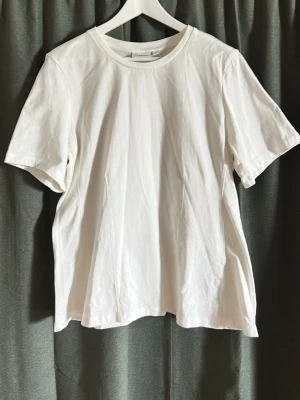 Vit basic t-shirt från KappAhl - En klassisk vit t-shirt från KappAhl i mjuk bomull. T-shirten har rund halsringning och korta ärmar, med en relaxed passform som passar till allt. Perfekt basplagg för garderoben.
