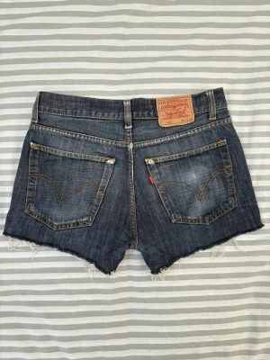 Levi's 501 blå shorts, storlek W30 L32 - Jeansshorts med fem fickor, bälteshällor och knäppning framtill. Shortsen har en obearbetad nederkant. Medelhög midja som lyfter rumpan så snyggt.