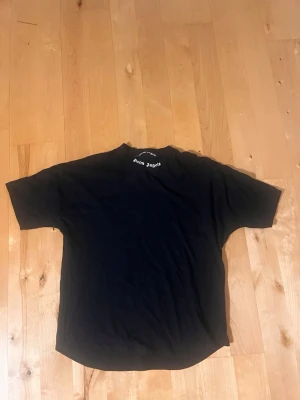 Svart Palm Angels t-shirt - Svart t-shirt från Palm Angels med vit logga tryckt i nacken. Klassisk rund halsringning och korta ärmar. Tillverkad i mjuk bomull för en bekväm känsla. Perfekt för en avslappnad streetwear-look. Passar br swim M/L