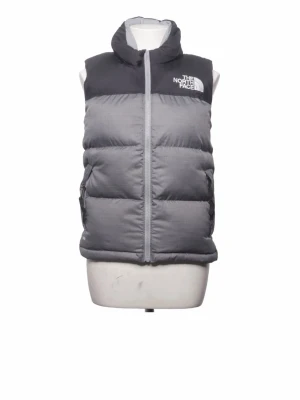 Grå dunväst från The North Face - Snygg och varm dunväst från The North Face i två nyanser av grått. Västen har hög krage, dragkedja framtill och två sidofickor. Klassisk logga på bröstet och ryggen. Perfekt för lager-på-lager och outdoor-stil.