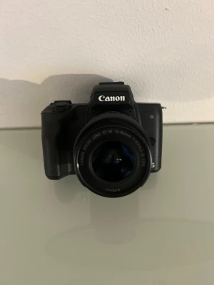 Canon EOS M50 systemkamera med vridbar skärm - Säljer en svart Canon EOS M50 systemkamera med ett 15-45mm objektiv. Kameran har en vridbar LCD-skärm som gör det enkelt att ta selfies eller filma vloggar. Smidig och modern design i tålig plast, perfekt för dig som vill ta snygga bilder och videos. Batteri och original laddaren tillkommer.