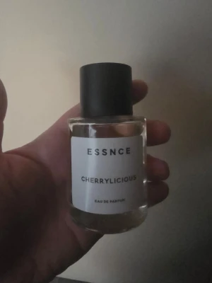 ESSNCE Cherrylicious Eau de Parfum - Cherrylicious från ESSNCE är en Eau de Parfum i en stilren, genomskinlig glasflaska med svart lock. Doften har inslag av körsbär och vanilj, och flaskan har en minimalistisk vit etikett med svart text. Perfekt för dig som gillar fruktiga och söta parfymer.