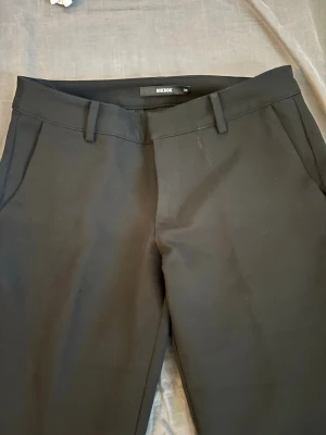 Svarta kostymbyxor från Bik Bok - Snygga svarta kostymbyxor från Bik Bok med klassiska fickor. Byxorna har hällor för skärp och en stilren look som passar till många olika outfits. Materialet känns mjukt och har en lätt stretch för extra komfort, dom är i petite modellen så därav lite kortare i längd.