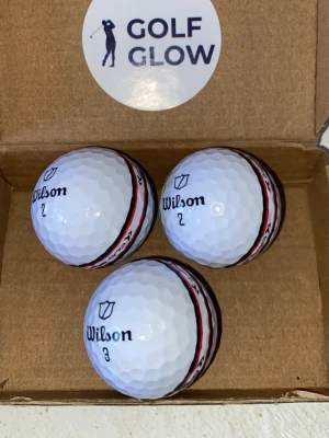 Wilsonstaff stripe 3-pack - Tre vita golfbollar från Wilson med en tydlig röd och svart rand runt mitten. Bollarna har märkningarna 2 och 3 samt Wilson-logga tryckt på ytan. Perfekta för dig som vill ha extra synlighet på golfbanan.