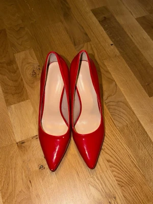 Röda lackpumps med spetsig tå - Snygga röda pumps i glansigt lackmaterial med spetsig tå och smal klack. Klassisk och elegant design som ger en cool statement-look. Insidan är ljusbeige och klacken är hög och smal för extra attityd.