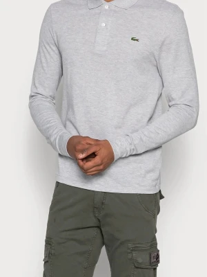 Grå långärmad skjorta från Lacoste - Klassisk grå långärmad skjorta från Lacoste med broderad krokodil på bröstet. Skjortan har en klassisk krage och knappar vid halsen. Tillverkad i mjukt bomullsmaterial och har en avslappnad passform. Aldrig använd köpte fel storlek..  säljer för 499