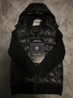 Svart cardiganjacka från Leon Marcél - Svart cardiganjacka från Leon Marcél. Jackan är stickad i 100% strechbar bomull förutom själva kroppen som är gjord i polyester. Jackan har borttagbar huva, dragkedja framtill och två fickor med dragkedja. Använd 3-4 ggr. NYPRIS: 1400kr. MITT PRIS: 899kr