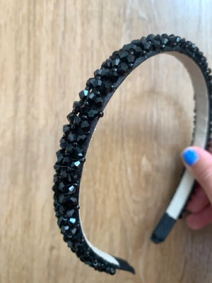 Svart diadem med glittrande pärlor - Snyggt svart diadem täckt med glittrande svarta pärlor som ger en lyxig och trendig känsla. Diademet har en klassisk form och är klätt i tyg med pärlor i plast som reflekterar ljuset. Perfekt accessoar för att lyfta din look.