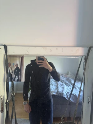 Svart hoodie från Ralph Lauren - Säljer en svart hoodie från Ralph Lauren med dragkedja framtill och klassisk vit logga på bröstet. Hoodien har huva med snören, två fickor fram och ribbade muddar vid ärmslut och nederkant. Perfekt för en chill och stilren look.