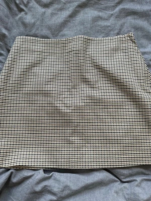  kortkjol från H&M - Snygg  kortkjol från H&M i beige, svart och vitt. Kjolen har en klassisk rak passform och är fodrad med ljus insida. Perfekt för dig som gillar tidlös stil och vill ha en kjol som funkar till många olika looks. Använt en gång. 