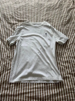 Vit t-shirt från Ralph Lauren - Klassisk vit t-shirt från Ralph Lauren med rund hals och korta ärmar. Diskret broderad logga i mörkblått på bröstet. Tillverkad i mjuk bomull för en skön och avslappnad look.